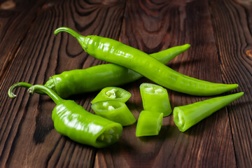 Green hot chili peppers with slices on wooden background