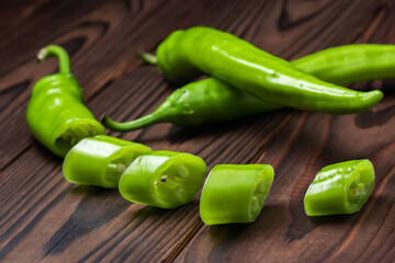 Green hot chili peppers with slices on wooden background