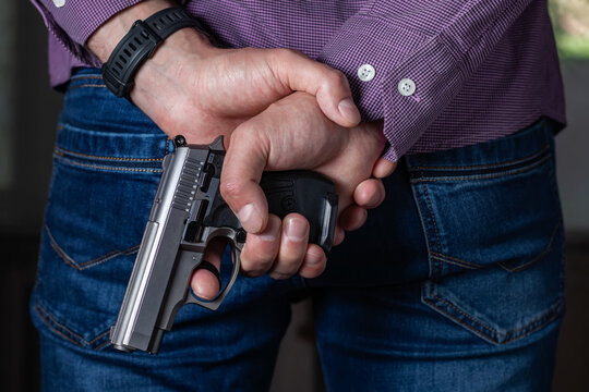 A man holding a gun in his hand behind his back, close-up view. Concepts: crime, attempted murder, a gunshot wound