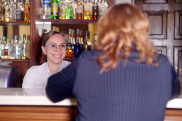 Cheerful bartender woman talking to client in cafe. Positive young female in casual clothes and...
