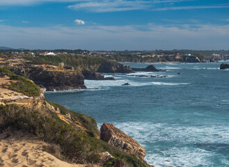 View over coastline with cliffs and rocks in the ocean towards village Vila Nova de Milfontes. Fishermans hiking trail at wild Rota Vicentina coast