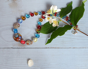 Murano glass necklace and jasmine (Philadélphus) flowers on a blue background, composition with women's jewelry, selective focus, horizontal format.