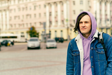 Young handsome man with dreadlocks in casual clothes posing on busy street in downtown.