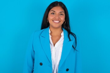 Young latin woman wearing  blue blazer blue background with a happy and cool smile on face. Lucky person.