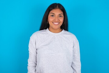 Fototapeta premium Young latin woman wearing gray sweater blue background with nice beaming smile pleased expression. Positive emotions concept