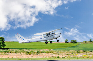 Fototapeta na wymiar Single engine ultralight airplane taking off from airfield under blue sky with white clouds