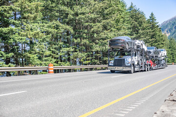Industrial car hauler big rig semi truck transporting cars on two level modular semi trailer running on the wide highway road in Columbia Gorge