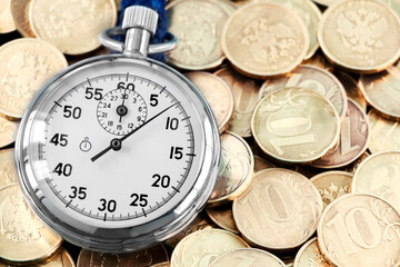 Analog stopwatch and pile of gold coins on a black background close-up. Counting time by stopwatch. Time measurement. Time management concept.A tool for measuring time.Dial stopwatch arrow