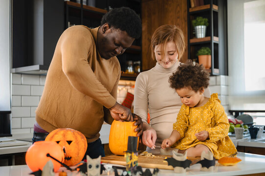 Multi-ethnic family with small child carving a pumpkin preparing it for Halloween holiday, making jack-o-lantern