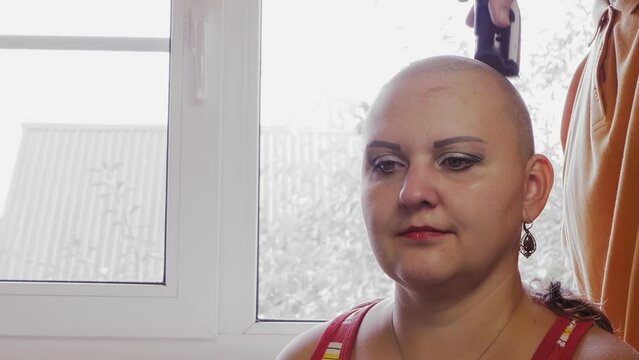 A man's hand shaves a woman's head with a clipper in the bathroom. Medium plan