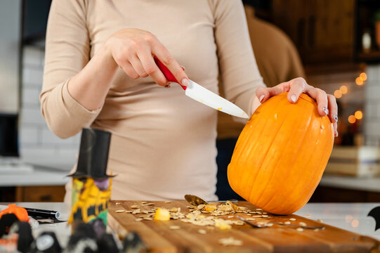Young woman carving a pumpkin, preparing it for the Halloween holiday, making jack-o-lantern