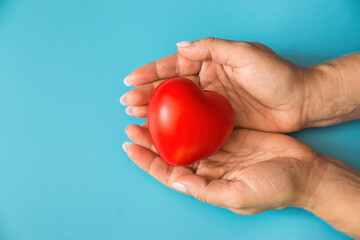 female hands hold a small red heart on a blue background. Women's health protection, cardiology and heart health concept. Mother's heart, love and care in the family