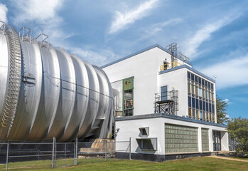Exterior of an aeronautical research wind tunnel and white stucco and glass block control building, daytime, sunny with clouds, nobody