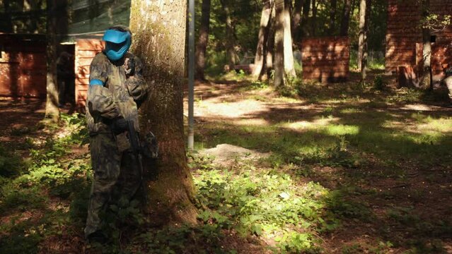 Paintball battle game being played with friends wearing camouflage and protective masks, leisure activity.