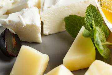 four types of cheese, feta, gorgonzola, parmesan, hard cheese, with honey on a plate, four types of cheese on a gray plate and black background