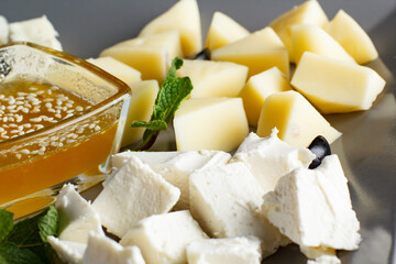 four types of cheese, feta, gorgonzola, parmesan, hard cheese, with honey on a plate, four types of cheese on a gray plate and black background