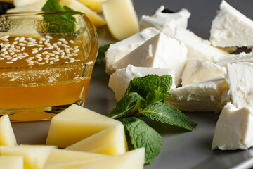 four types of cheese, feta, gorgonzola, parmesan, hard cheese, with honey on a plate, four types of cheese on a gray plate and black background