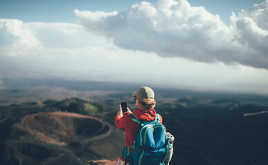 Rear view of woman backpacker taking photo with smart phone