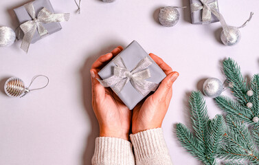 Female hands hold a gift box with a shiny ribbon on a gray background with a New Year's decor