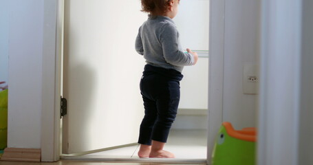 Fototapeta na wymiar Baby standing by home bathroom, one year toddler stands observing
