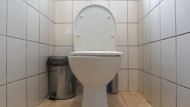 Toilet room interior with white toilet bowl, metallic wastebasket and white wall tiles