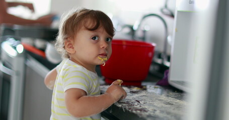 Baby playing covered with flour at kitchen, infant doing a mess with dough cooking