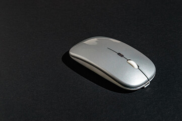 a computer mouse of silver color on a natural black background with hard light and shadow