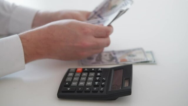 Budget money. Counting man. Payment spending. Unrecognizable guy using calculator spreading cash dollars on piles sitting light room interior.