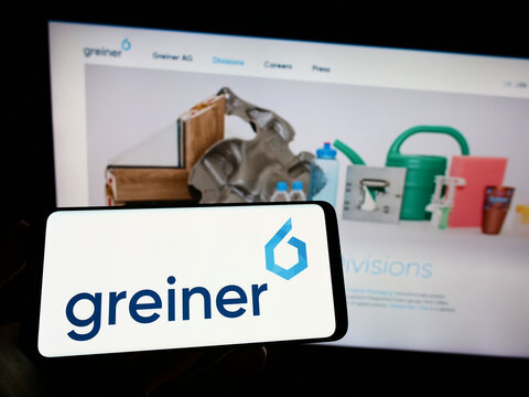 Stuttgart, Germany - 09-11-2022: Person holding mobile phone with logo of Austrian plastics company Greiner AG on screen in front of business web page. Focus on phone display.