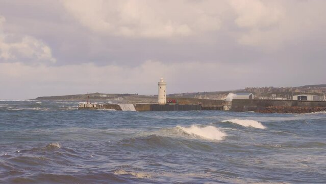 A footage scenic lighthouse at the Buckie, Moray, Scotland port entrance during a major storm with big waves crashing on it under a grey stormy sky	
