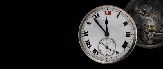 An old antique clock with roman numerals on the dial and clockwork isolated on black background