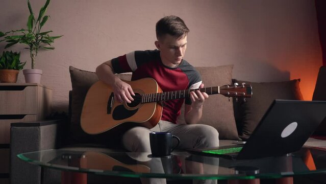 young man is learn.ing to play the acoustic guitar. online learning.
