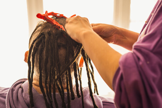 Unrecognizable person braids dreadlocks for man in salon. Faceless professional hairstylist makes hairstyle for client. Close up.