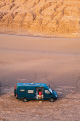 Woman sitting in her campervan in the desert at sunset