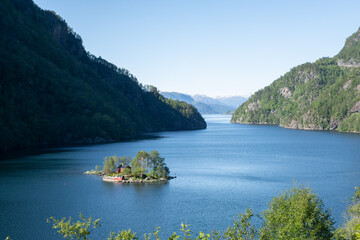 Wonderful landscapes in Norway. Beautiful scenery of a island with a red house on the Lovrafjorden fjord. Mountains with snow in background. Sunny day. Selective focus