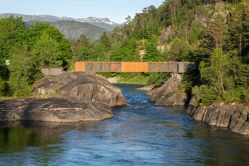 Fototapeta na wymiar Sand, Norway - June 6, 2022: Wonderful landscapes in Norway. Hose Bru, the metal bridge is a pedestrian bridge in the village of Sand (Suldal). The bridge spans the Sudalslagen river Sunny spring day