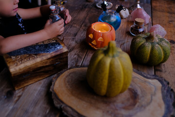 pumpkins, candles, little female witch prepares witch's potion, magic items on the table, funny chemical experiments in dark room, concept of Halloween party, family role-playing games