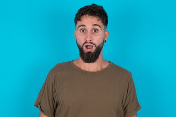 Shocked young bearded hispanic man wearing casual clothes over blue background stares bugged eyes keeps mouth opened has surprised expression. Omg concept