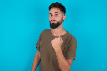 young bearded hispanic man wearing casual clothes over blue background shows fist has annoyed face expression going to revenge or threaten someone makes serious look. I will show you who is boss