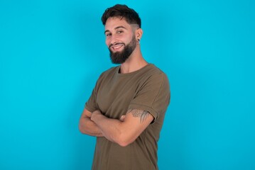 Portrait of young bearded hispanic man wearing casual clothes over blue background standing with folded arms and smiling