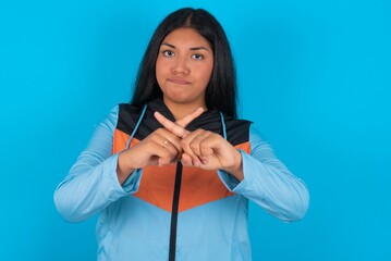 young beautiful latin woman wearing sportswear has rejection angry expression crossing fingers...