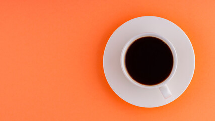 Cup of coffee on orange background. White cup of black coffee on a white saucer. Copy space. Top view