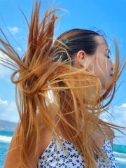 A girl with long red hair gathered in a ponytail enjoys nature on the beach during the wind.  Close-up portrait of a girl with freckles