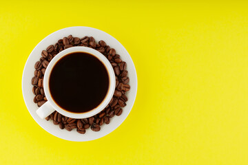 Coffee cup and roasted coffee beans on a saucer. Cup of black coffee on a yellow background. Top view. Copy space