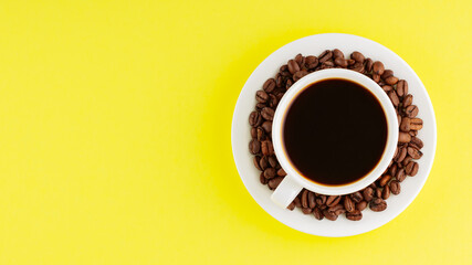 Coffee cup and roasted coffee beans on a saucer. Cup of black coffee on a yellow background. Top view. Copy space