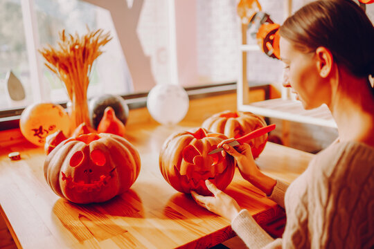 Young woman carving pumpkins for hallowee. Halloween, decoration and holidays concept.