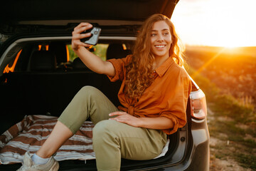 Selfie time. Young woman making selfie and enjoying sunset in the car. Lifestyle, travel, tourism,...