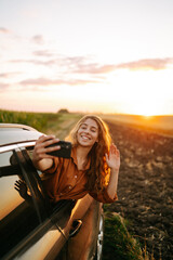 Selfie time. Young woman making selfie and enjoying sunset in the car. Lifestyle, travel, tourism, nature, active life.