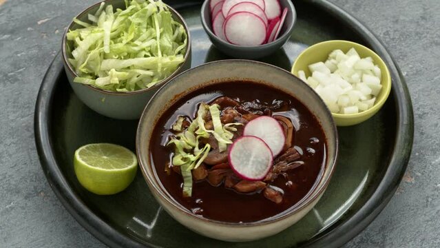 Vegan Pozole Rojo with lettuce, radish and onion. Famous Mexican cuisine dish made with cacahuazintle, shredded jackfruit, mushrooms and dried chilies: guaillo, ancho, pasilla.