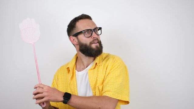 Young caucasian charismatic man holding a fly swatter wanting to kill annoying mosquito or a fly.